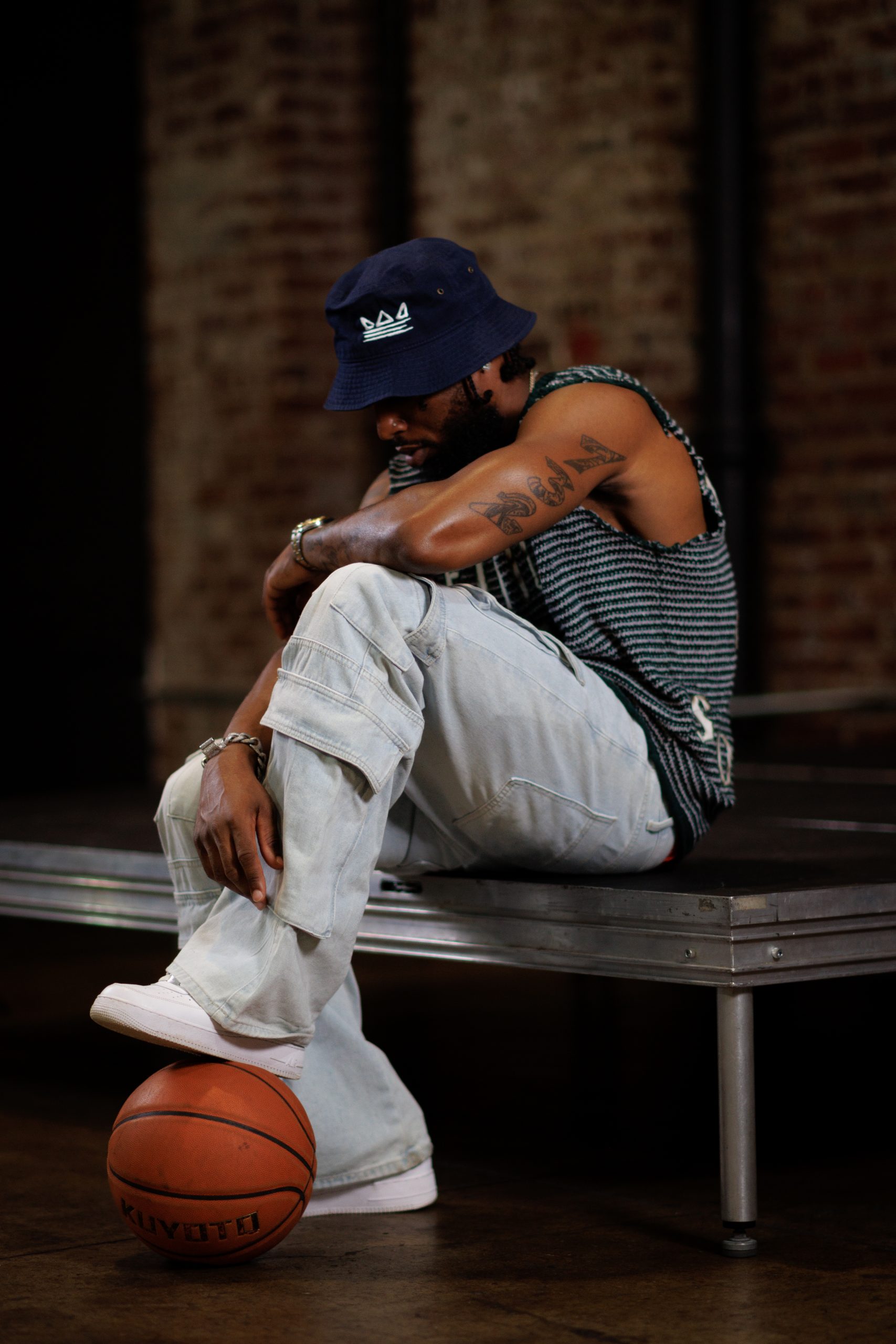 Man in streetwear leaning forward, seated, one foot on a basketball