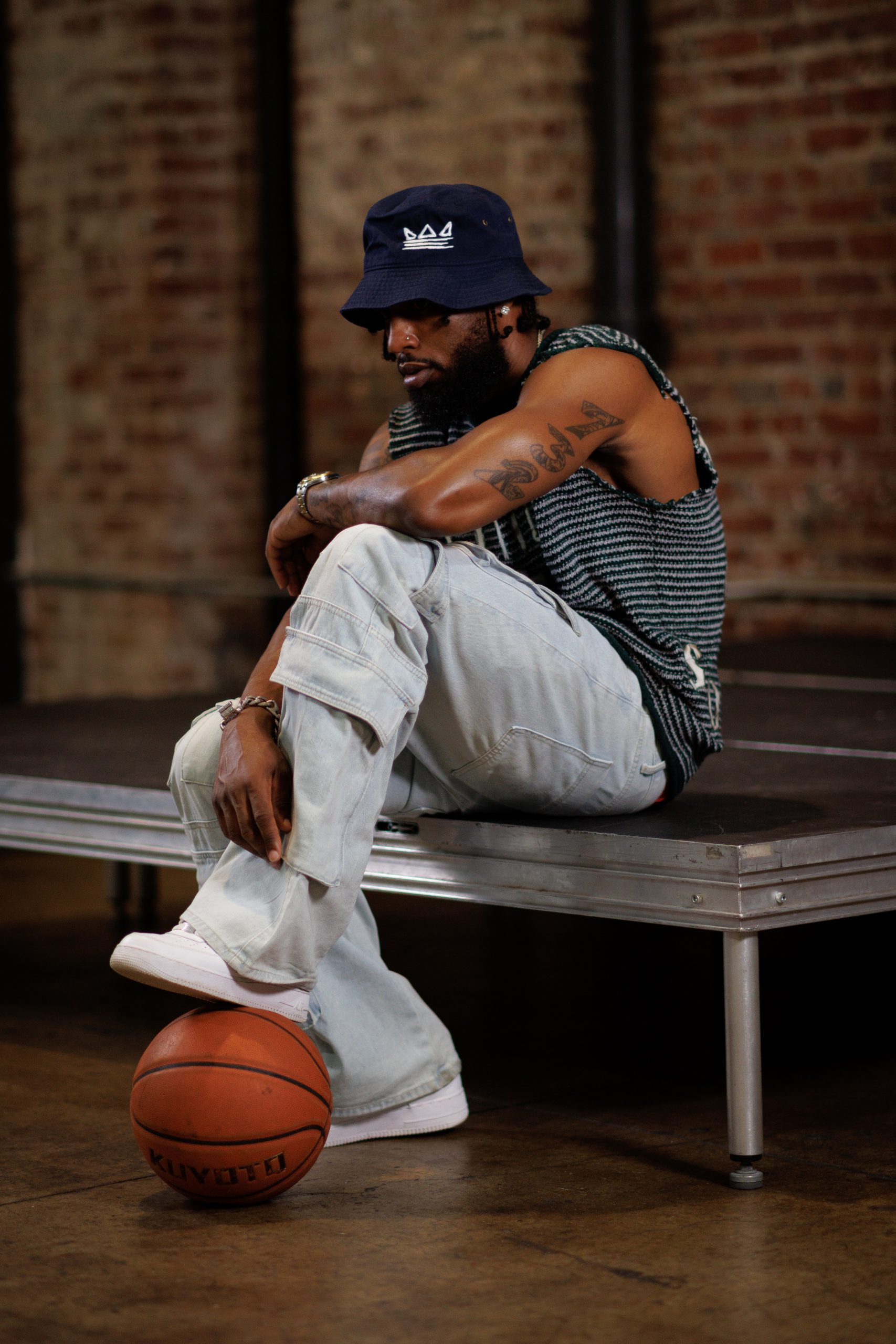 Man in streetwear seated on a bench, side profile, one foot on a basketball