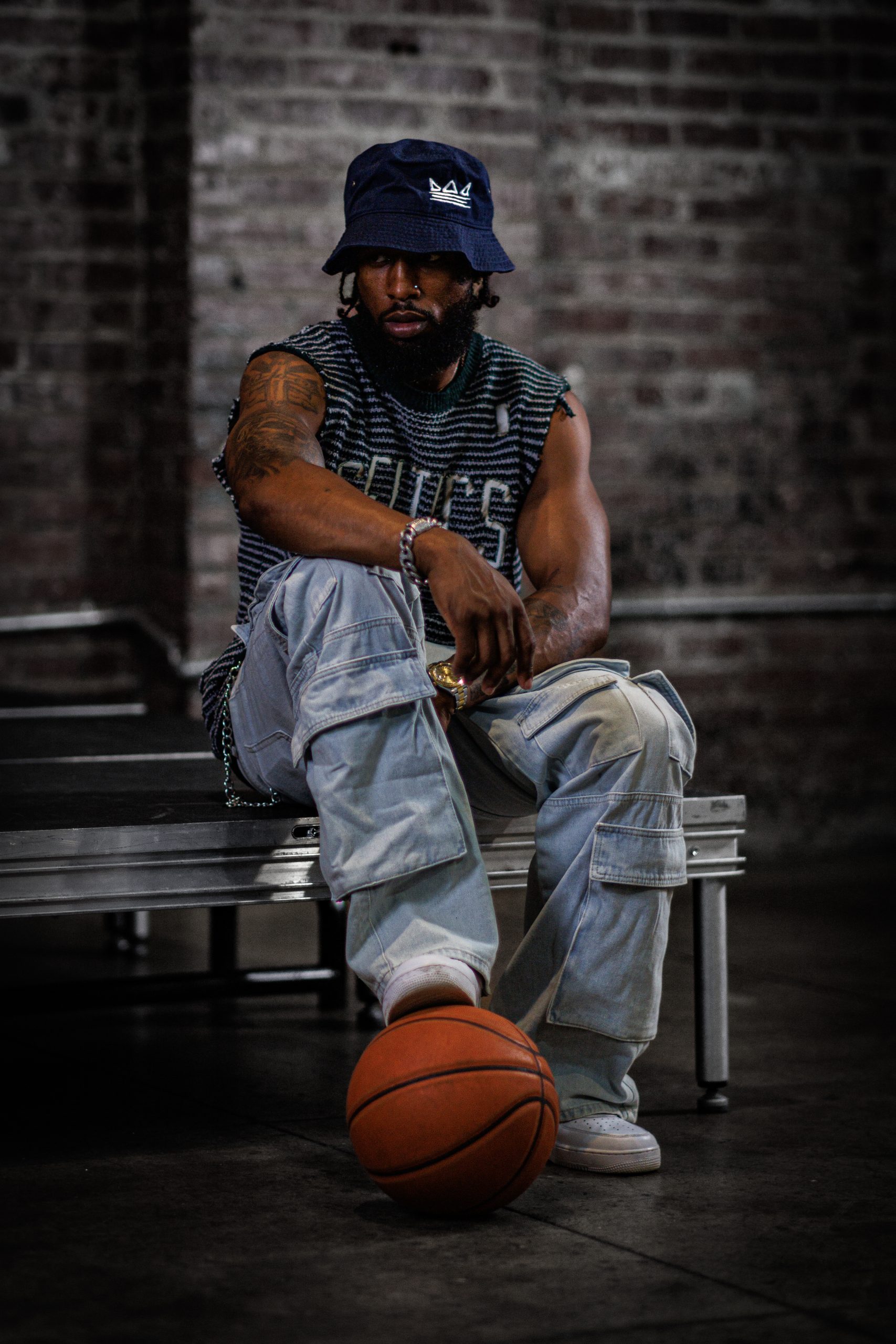 Man in streetwear and a bucket hat, one foot resting on a basketball
