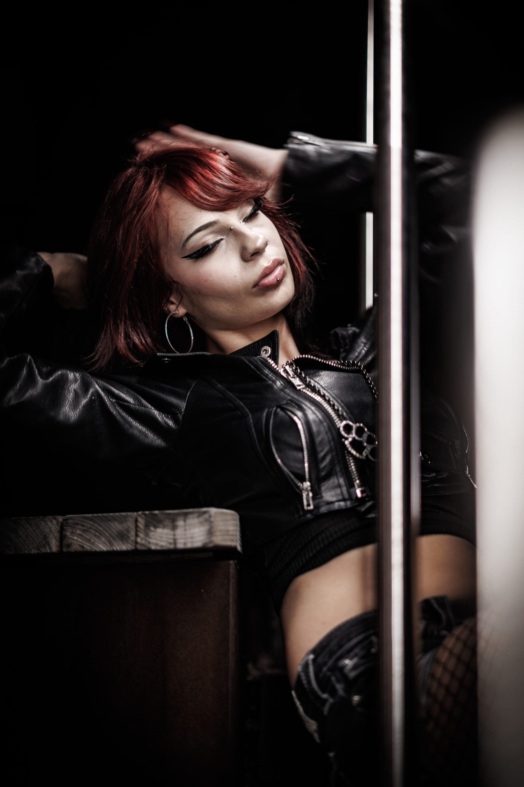 Woman with red hair in a leather jacket, eyes closed, moody low-key portrait
