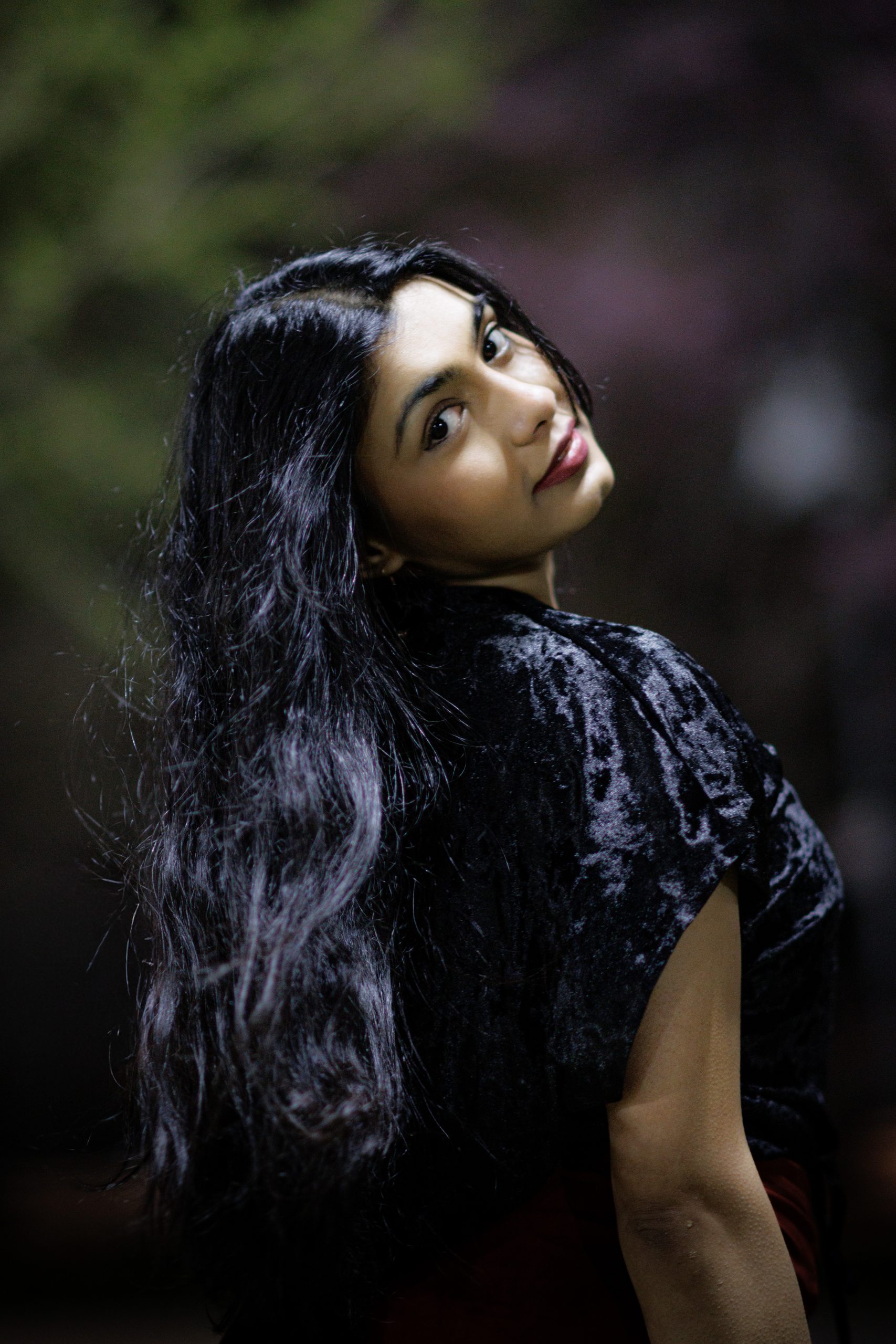 Woman with long dark hair looking back over her shoulder, black velvet top, night