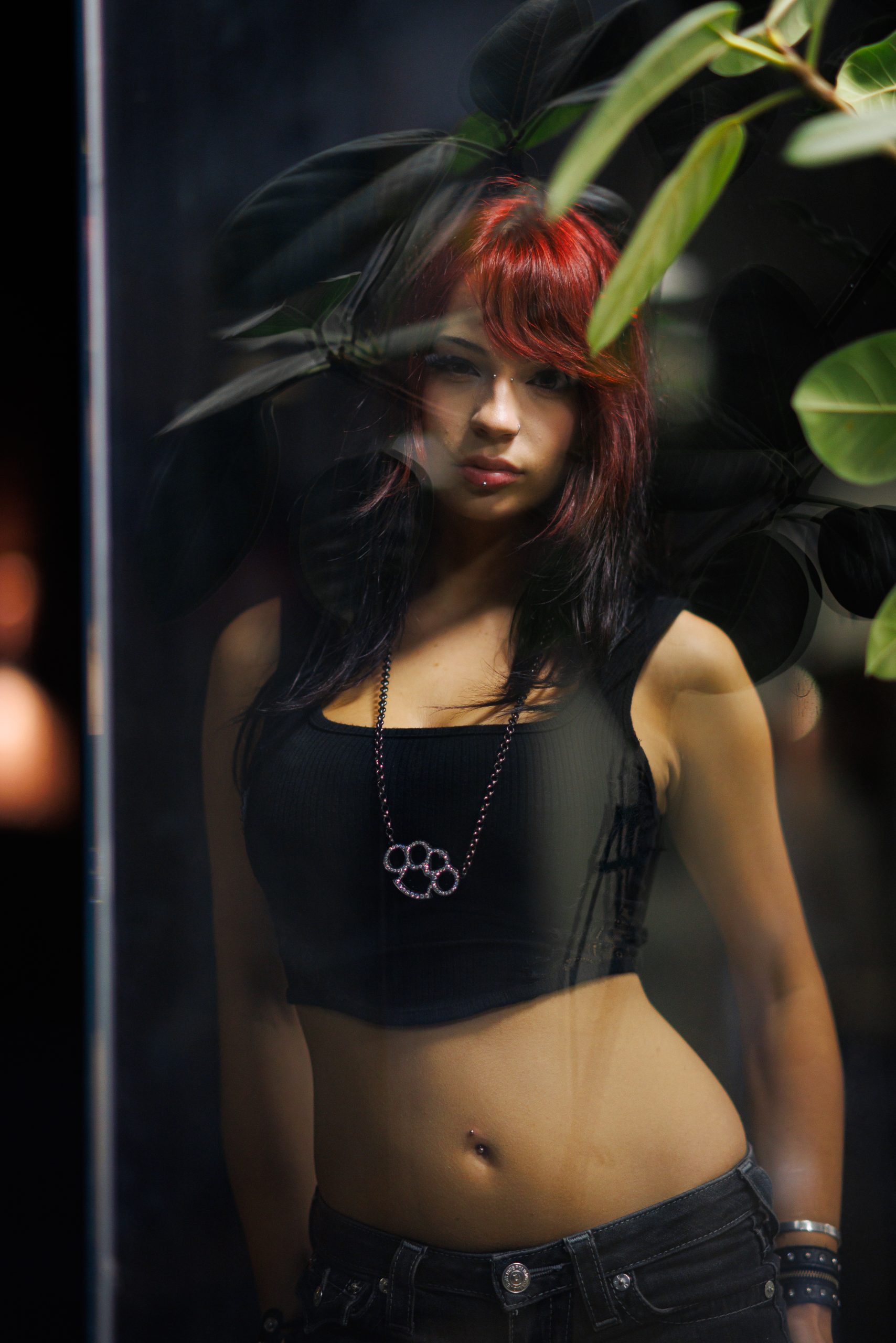 Woman with red hair seen through glass and leaves, moody reflection