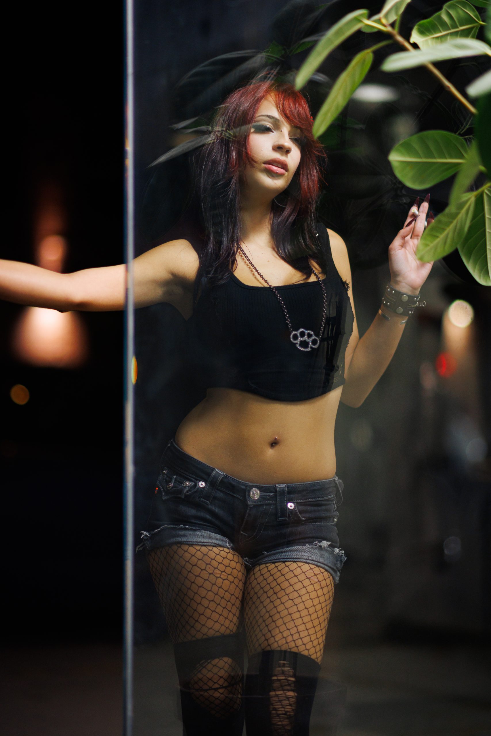 Woman with red hair holding a cigarette, reflected in glass with foliage