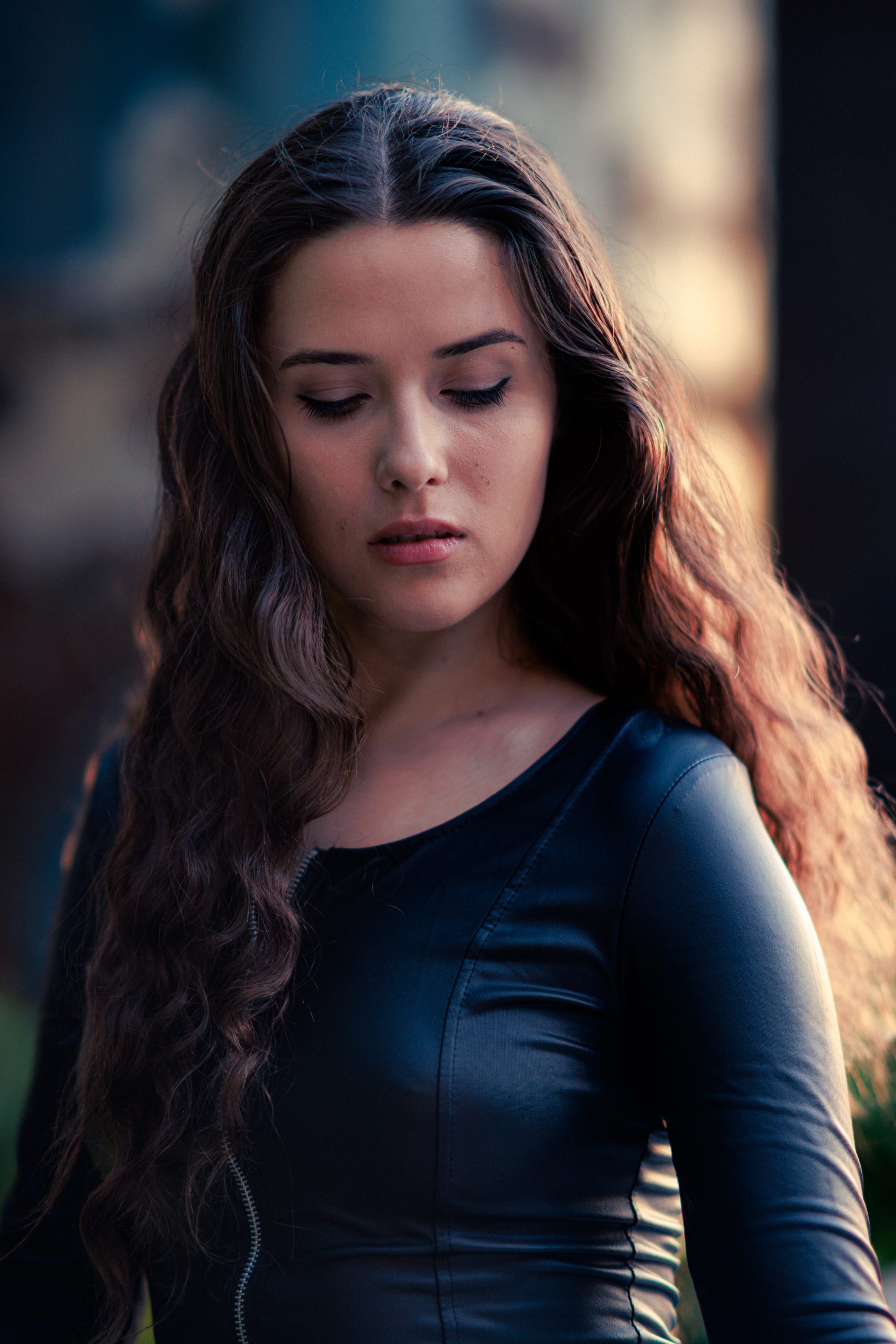 Woman with wavy hair in a black leather top, looking down, warm directional light