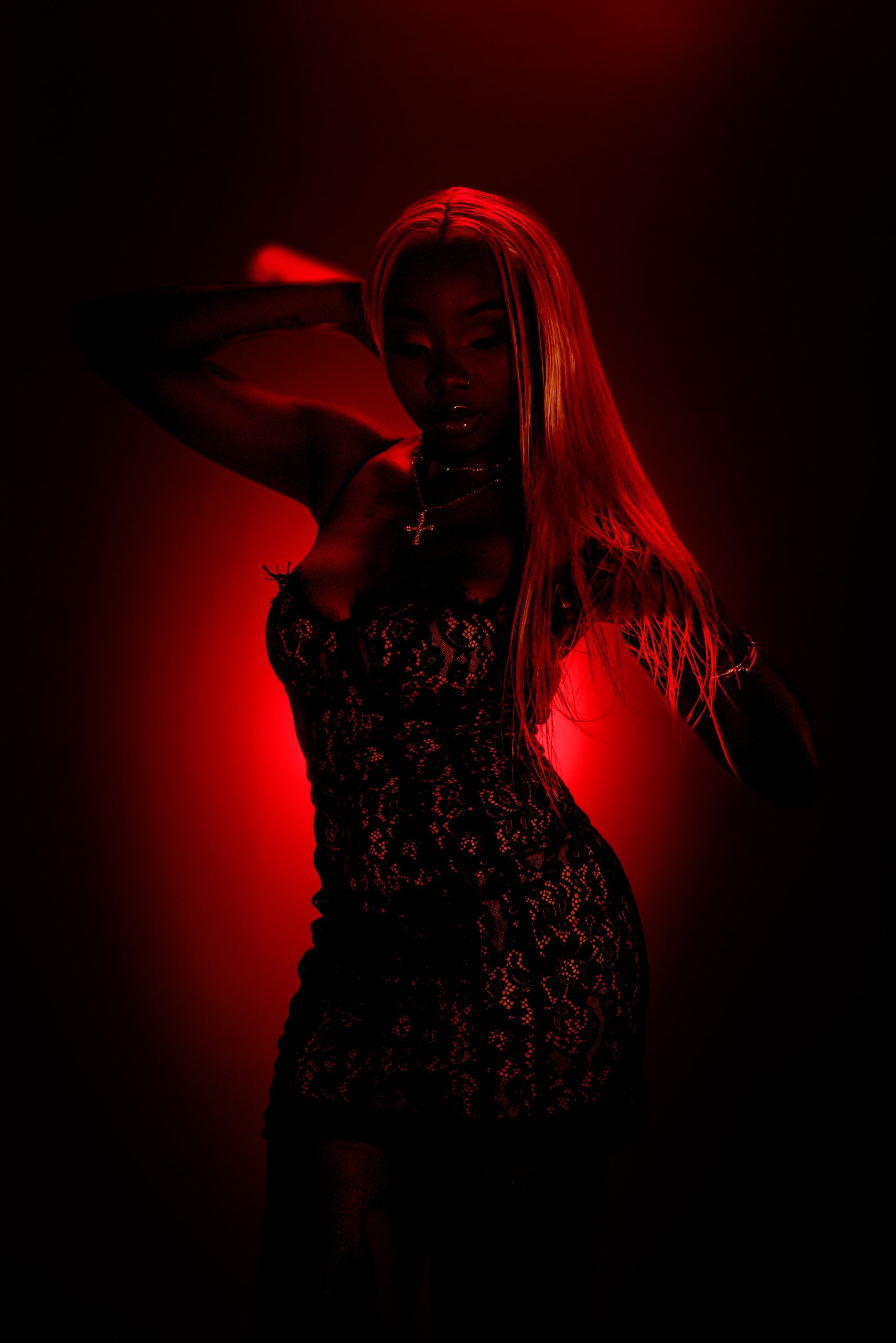 Silhouetted woman in a lace dress under dramatic red lighting, one hand raised