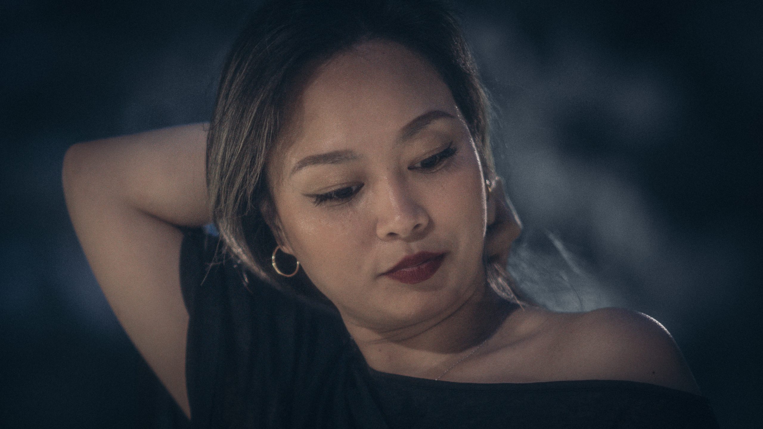 Close portrait of a woman with hand near her neck, dark moody lighting, red lipstick