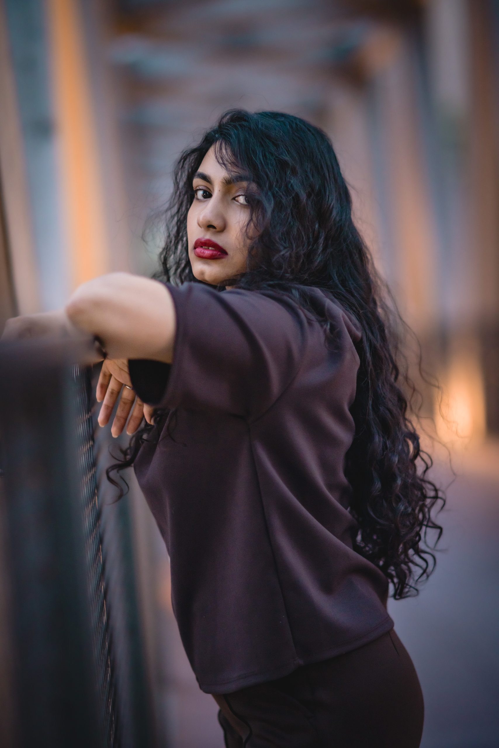 Woman reaching back over her shoulder in a purple top, warm string-lit alley