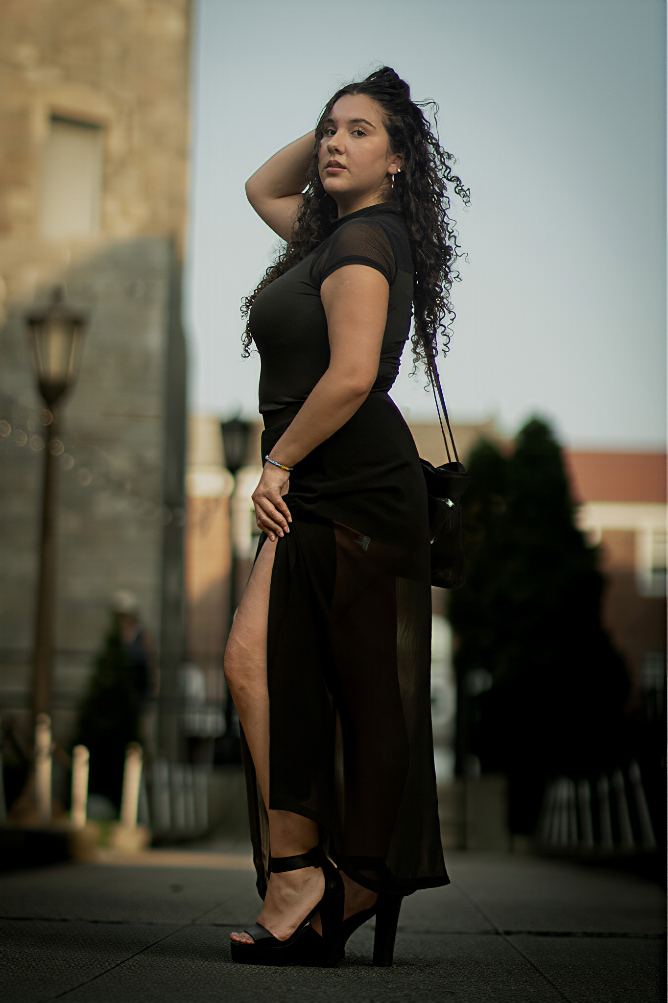 Woman in a black sheer-panel dress in an urban plaza, looking over her shoulder