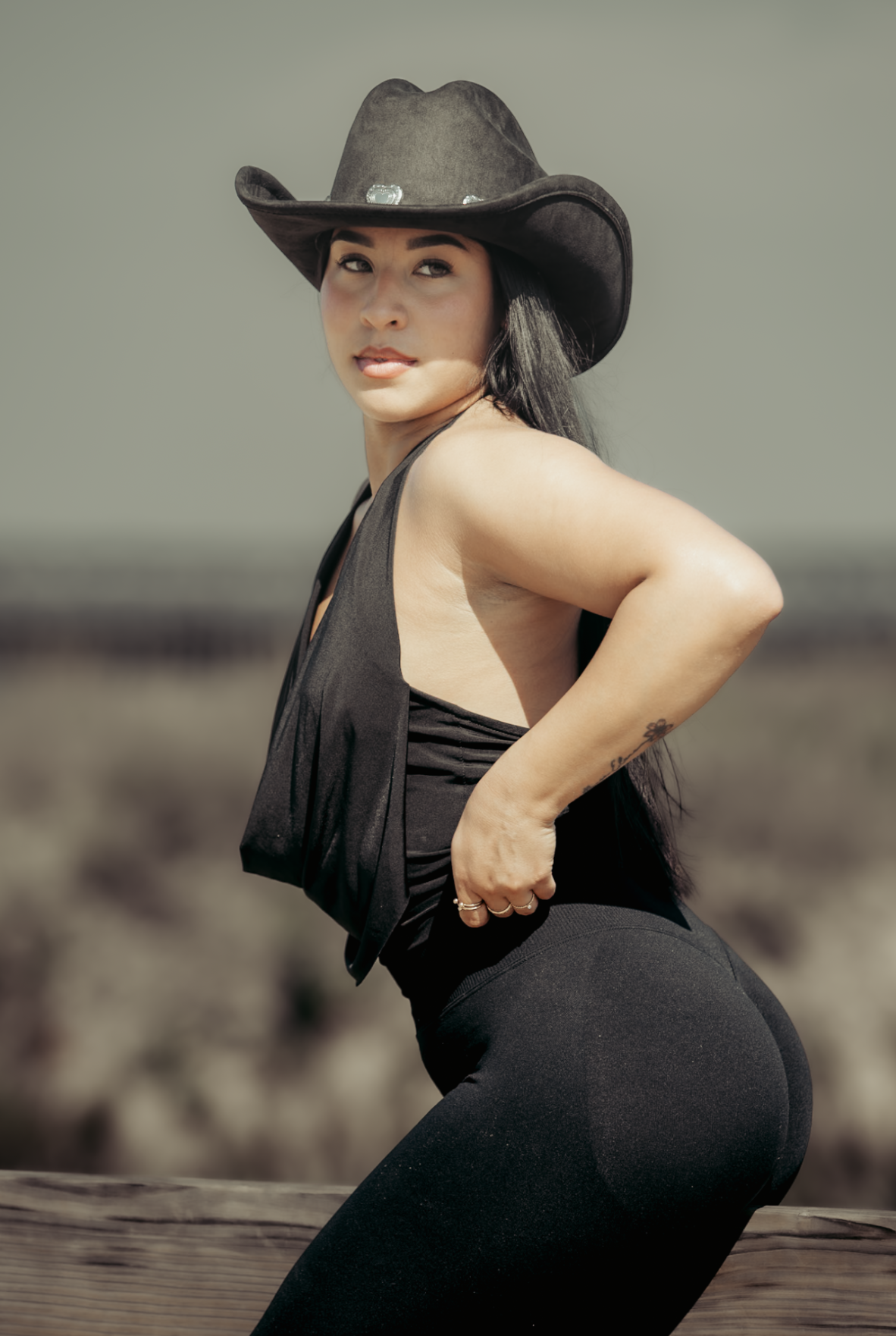 Woman in a black cowboy hat, looking back over her shoulder, desert landscape