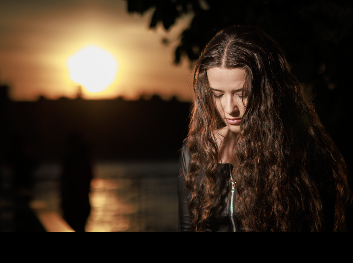 Woman with curly hair in a black leather outfit, golden hour by the water