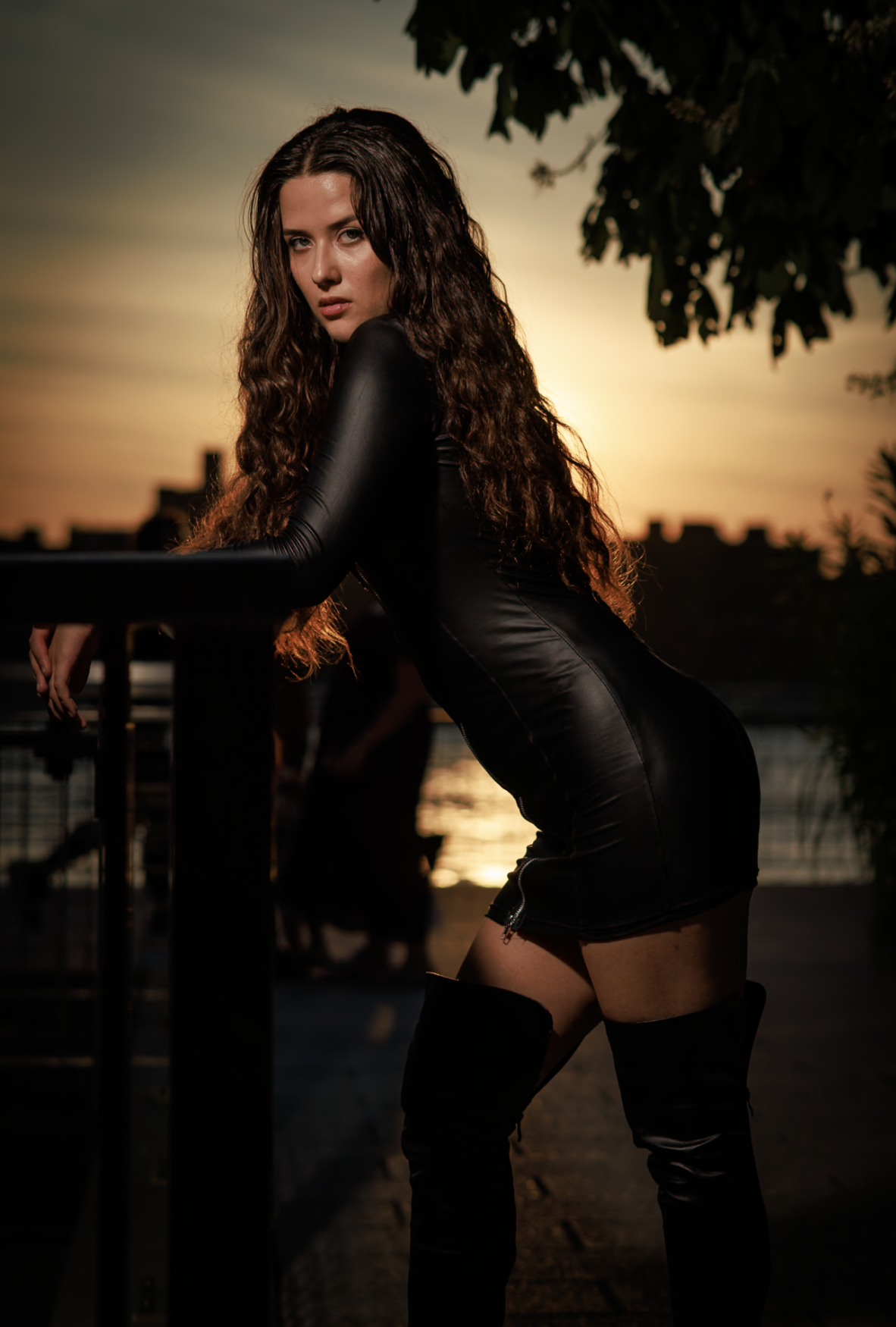 Woman with curly hair in a black leather outfit, golden hour by the water