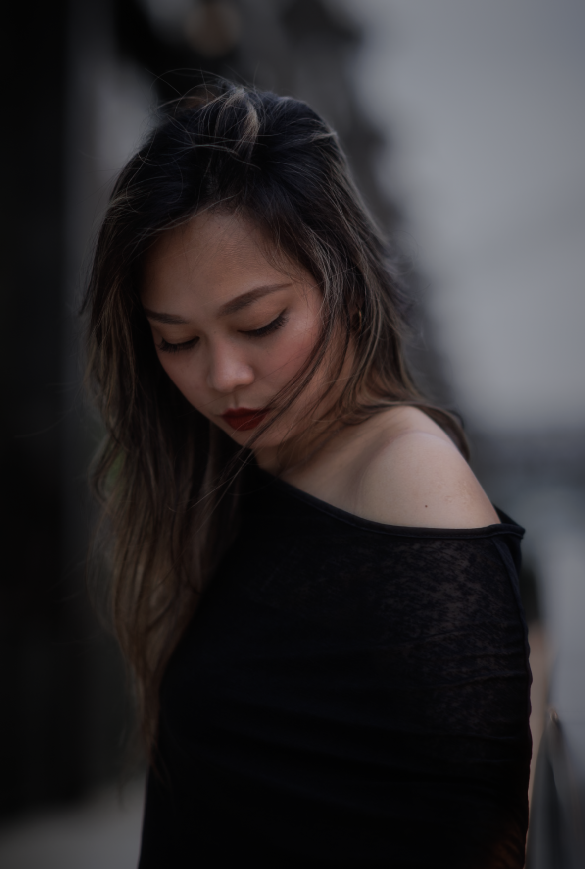 Woman with red lipstick in an off-shoulder black top, looking downward, soft light
