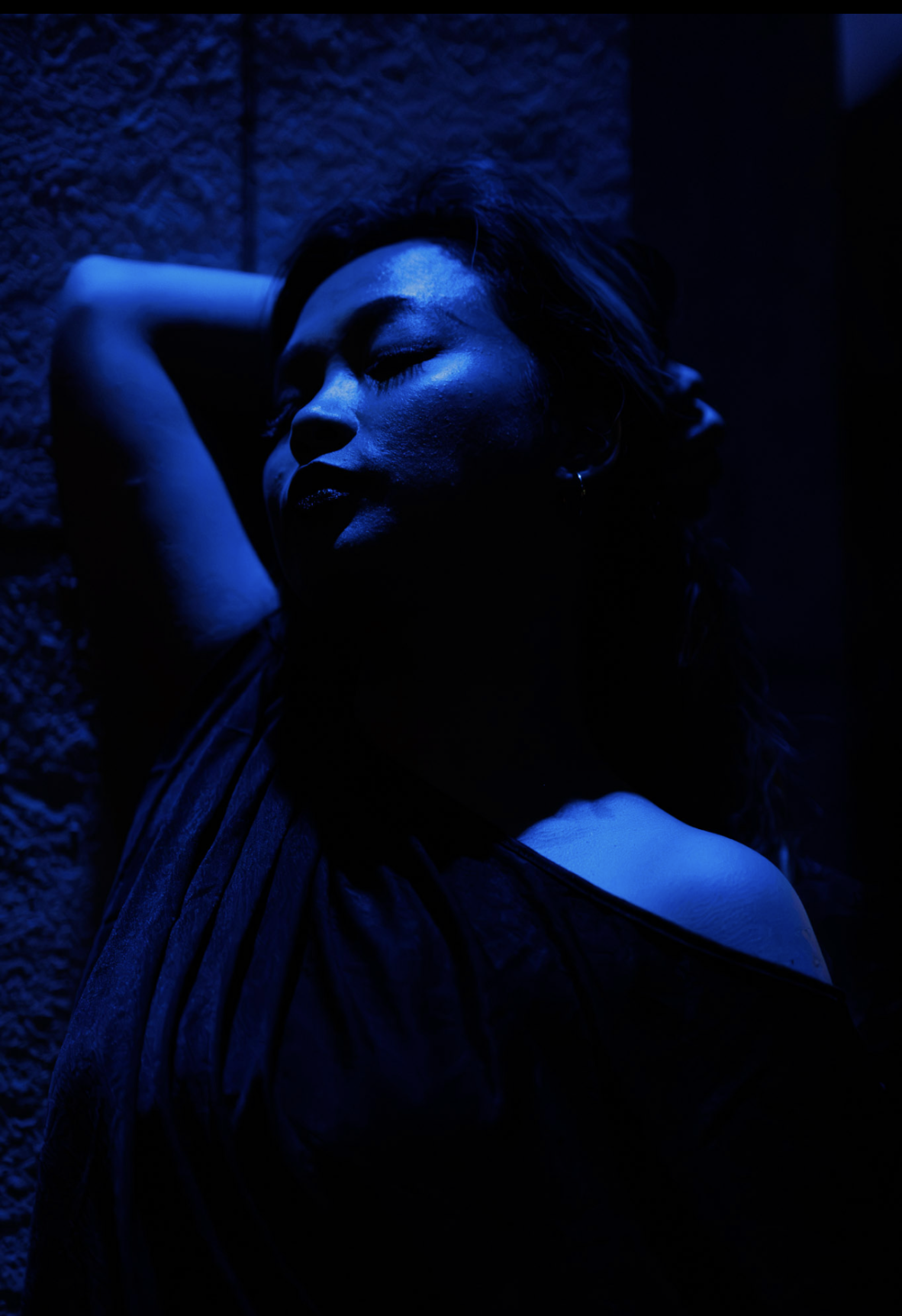 Woman in an off-shoulder black top against a stone wall, blue evening light