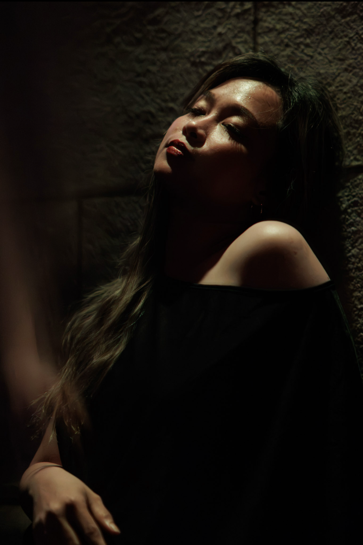 Close portrait of a woman in an off-shoulder black top, eyes closed, amber light