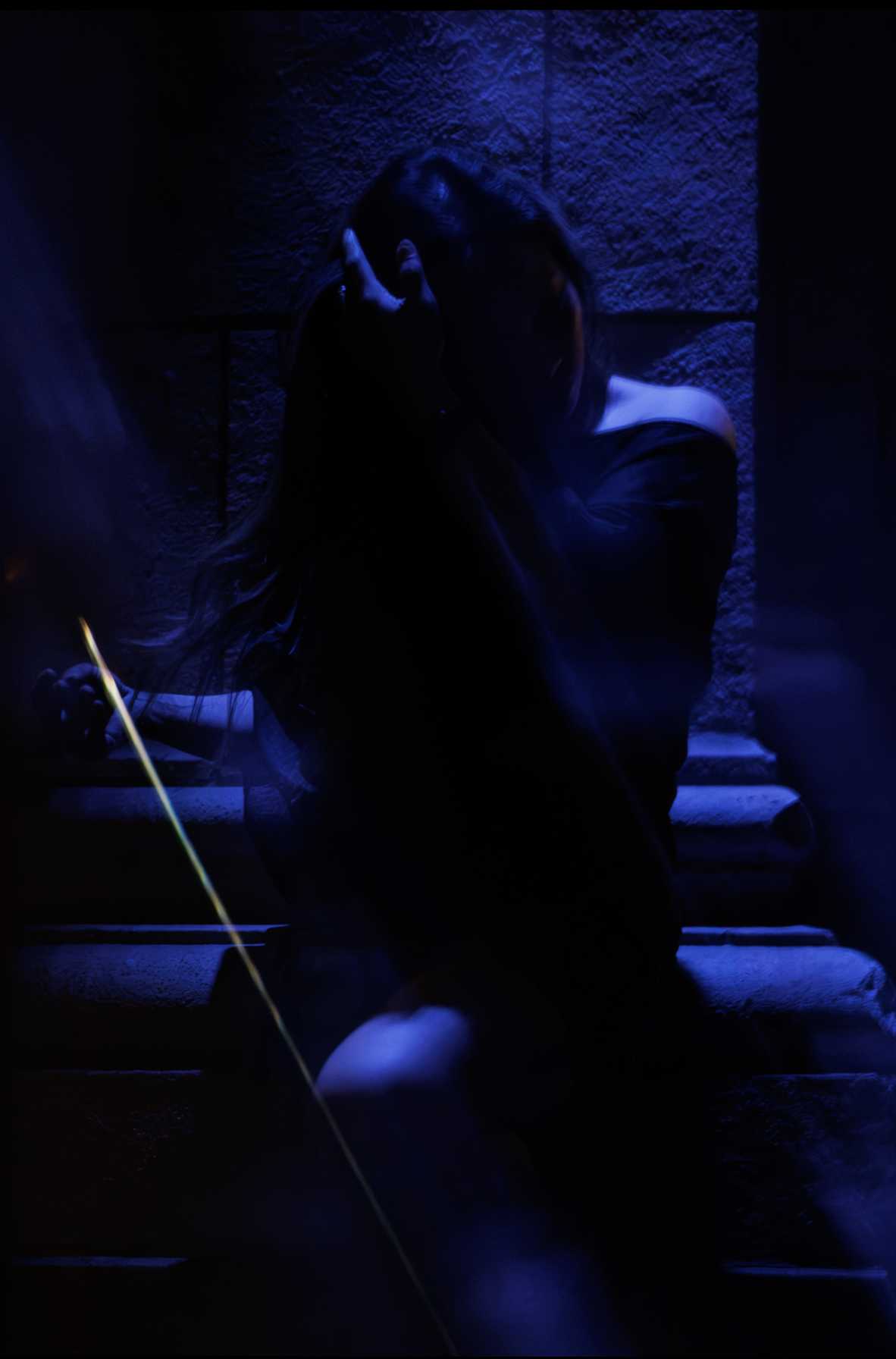 Woman with arm raised against a stone wall, low light