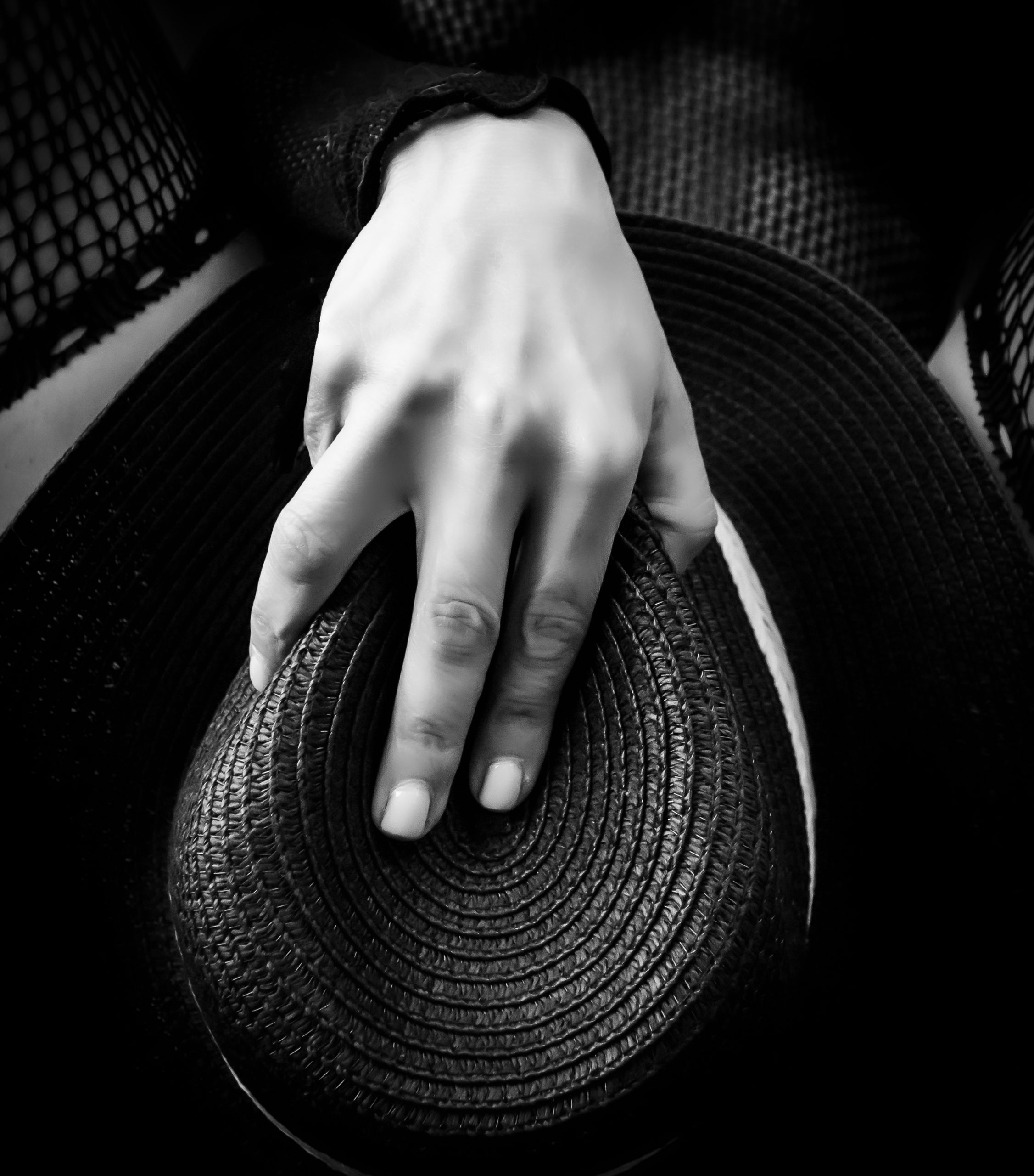 Close-up of a hand resting on a woven black hat, black and white
