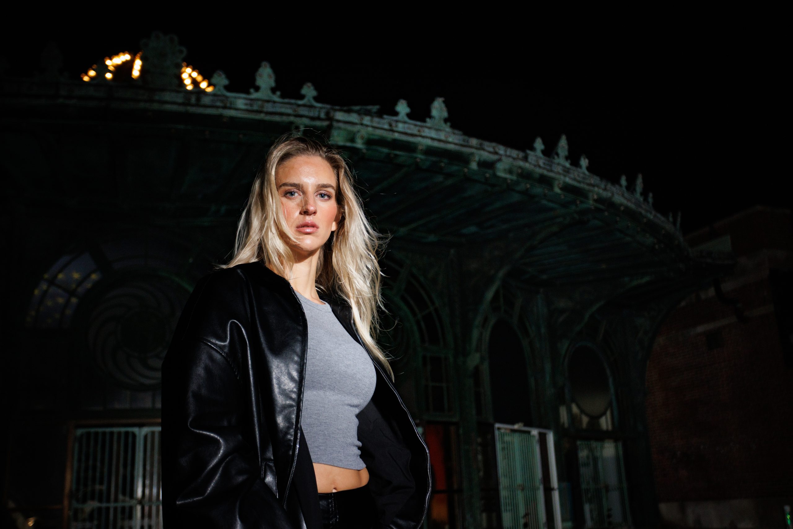 Woman in a leather jacket before an ornate illuminated structure at night