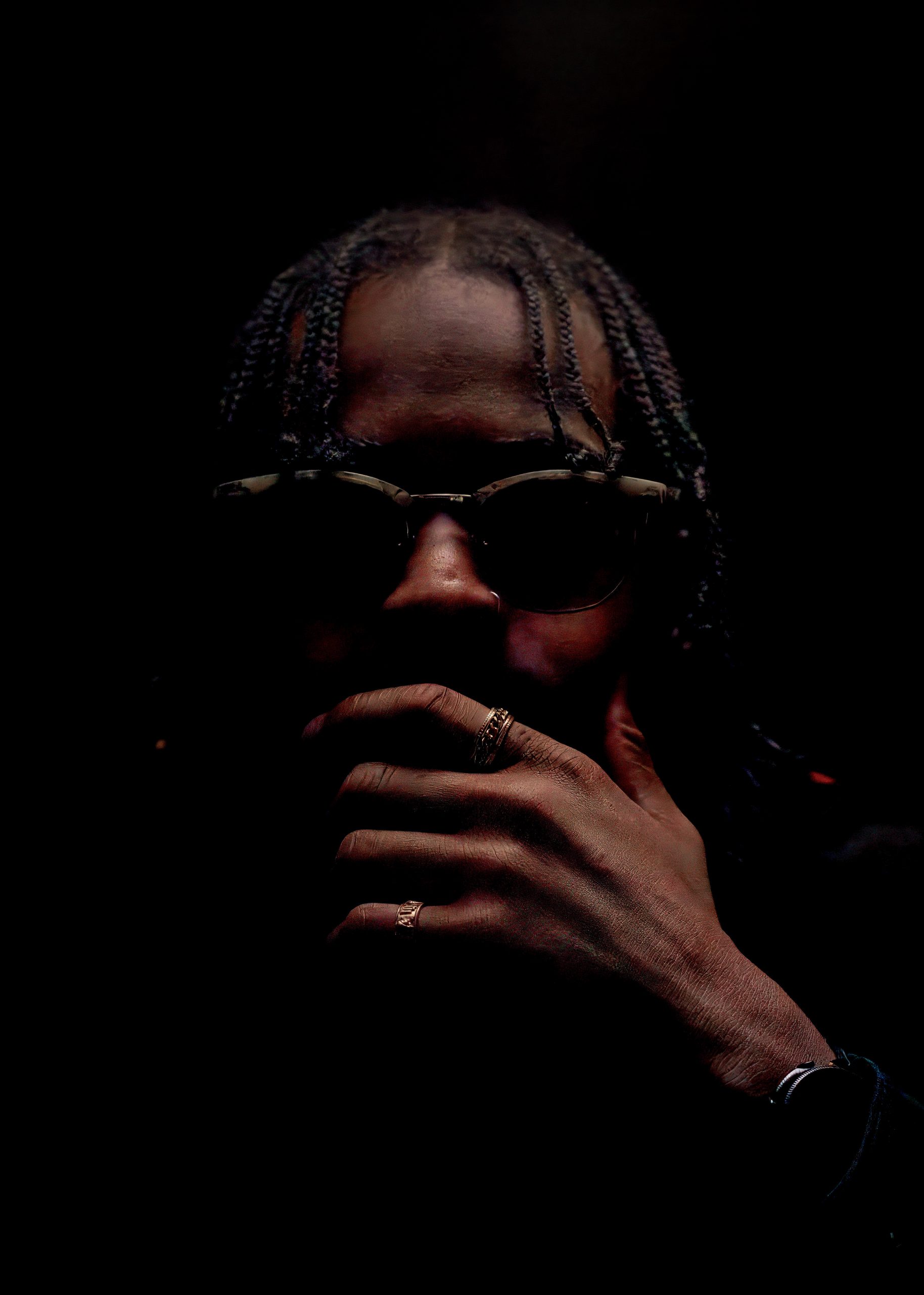 Close portrait of a man in sunglasses, hand near his chin, low-key lighting